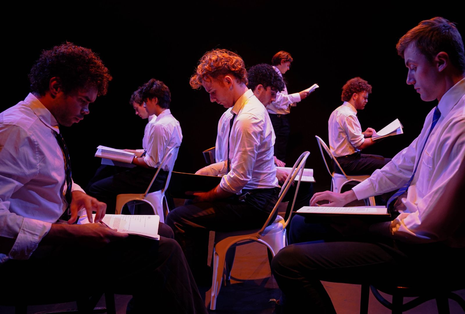 The cast of ALL BOYS are on NIDA's stage in school uniforms. They are seated, facing different ways and reading papers.