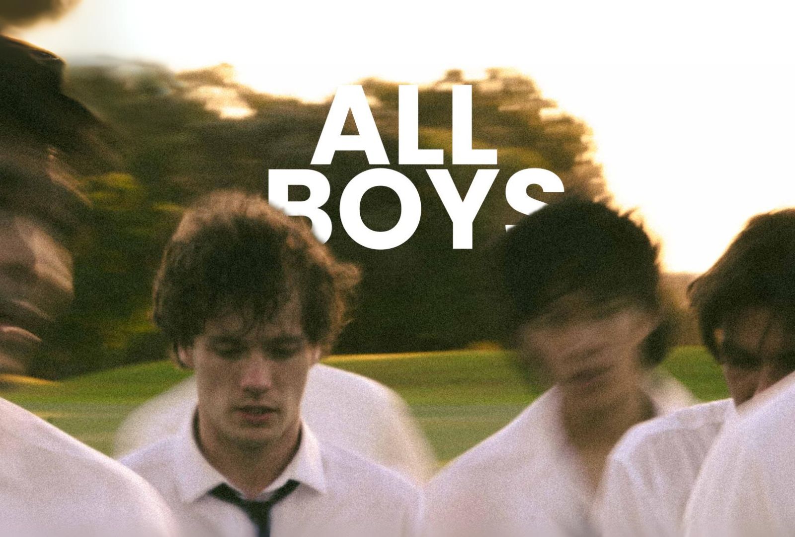 The hero image for ALL BOYS with the title written in white text behind five boys. The photo is grainy and the faces of each boy is blurry as they walk across a green field of grass.