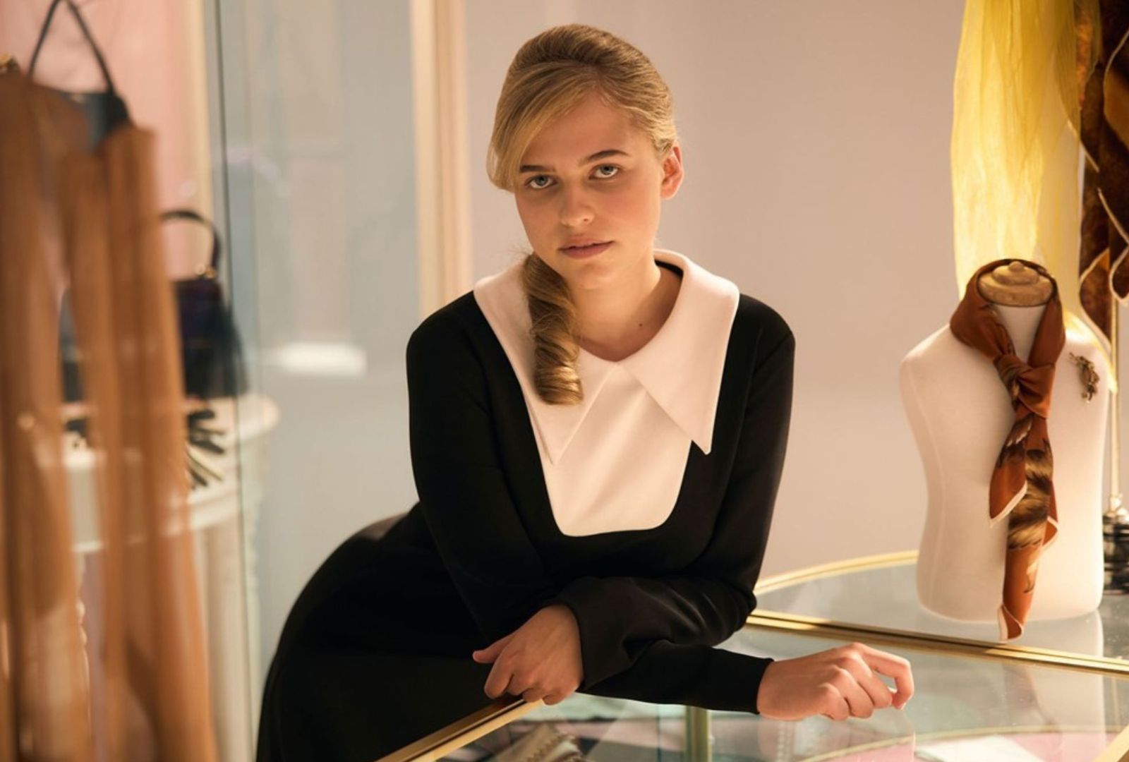 Clare Hughes is leaning on a glass table in a black dress.