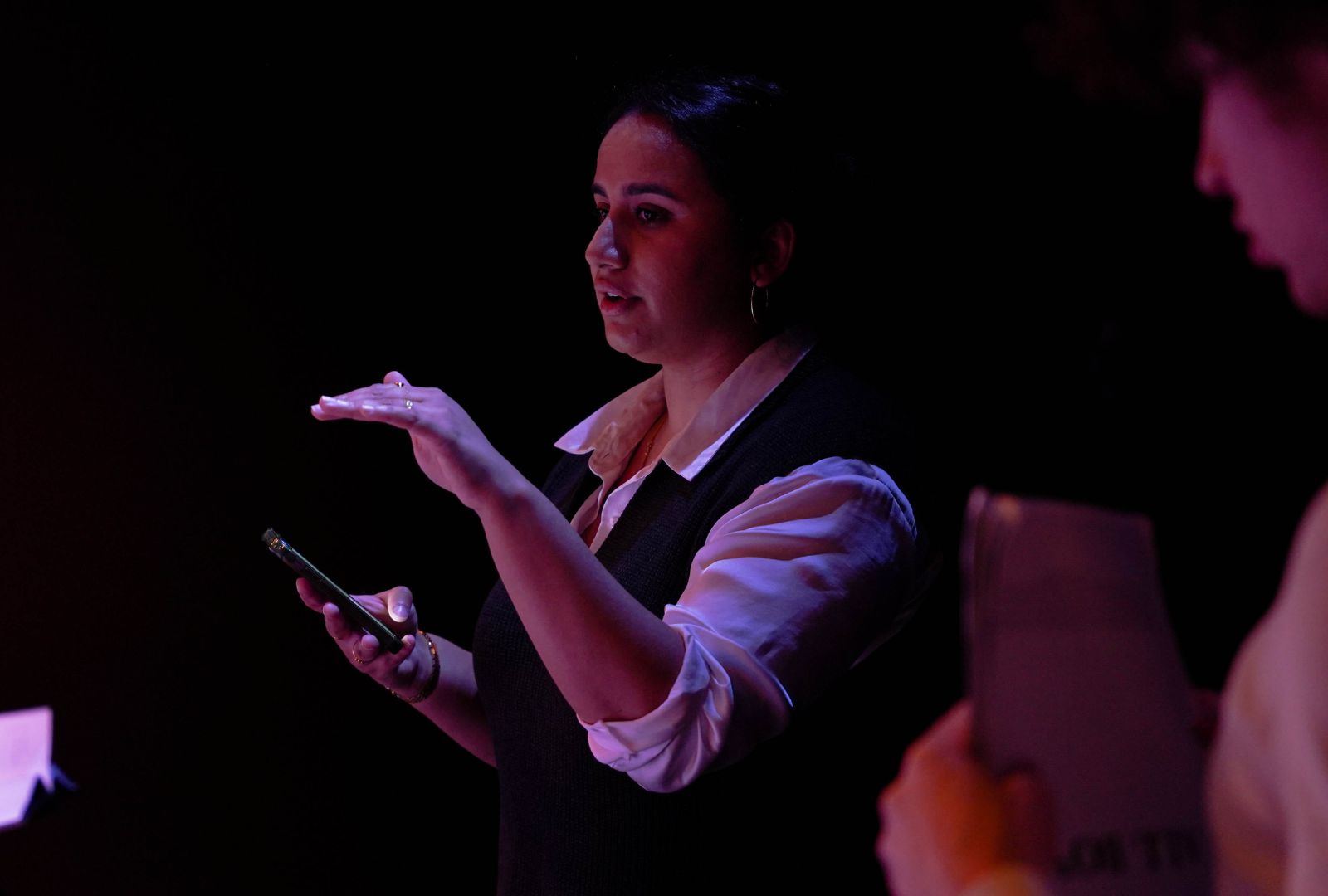 Mehhma Malhi stands in the dark holding her phone, giving the cast of ALL BOYS direction.