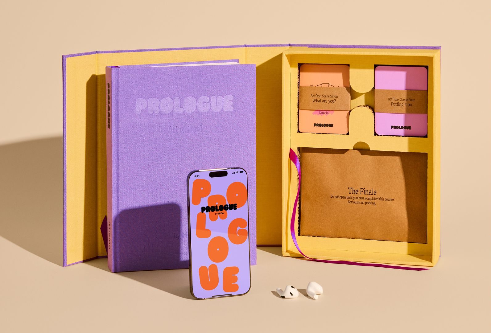 The Prologue by NIDA product opened with a beige background and a phone open to the Prologue app. Inside there is the Prologue book, two sets of cards and a brown envelope with 'The Finale' written on it.