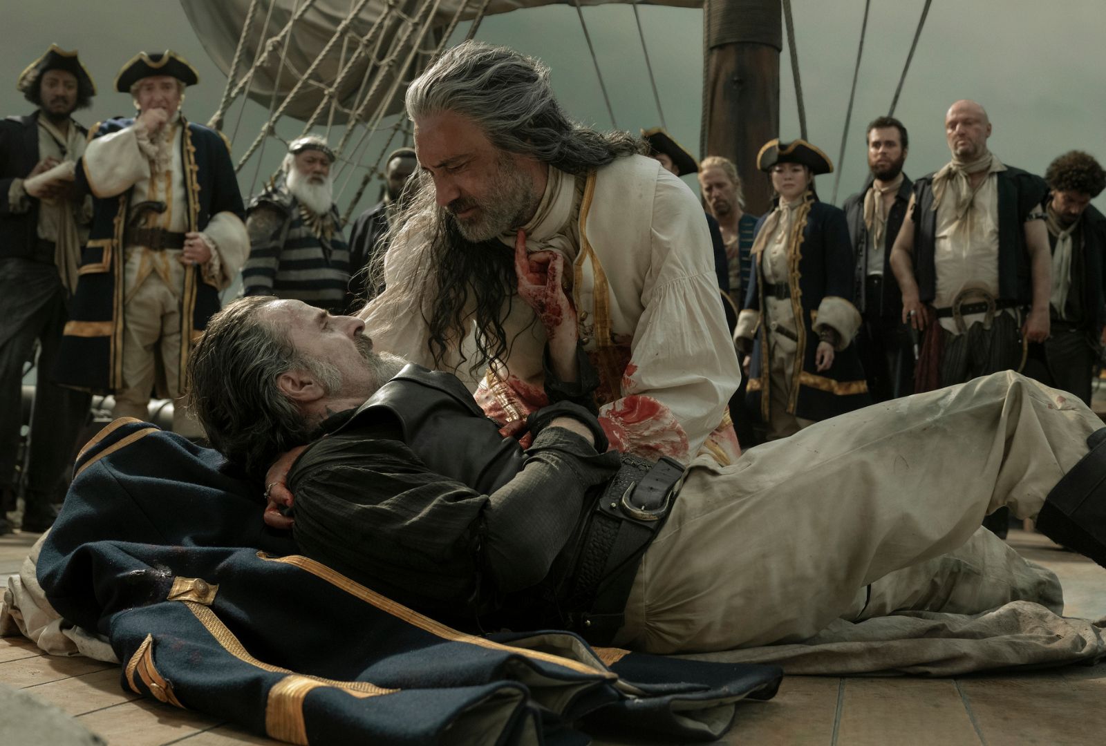 Con O'Neill and Taika Waititi in 'Our Flag Means Death'. Taika leans over Con as he passes away, surrounded by a pirate crew.