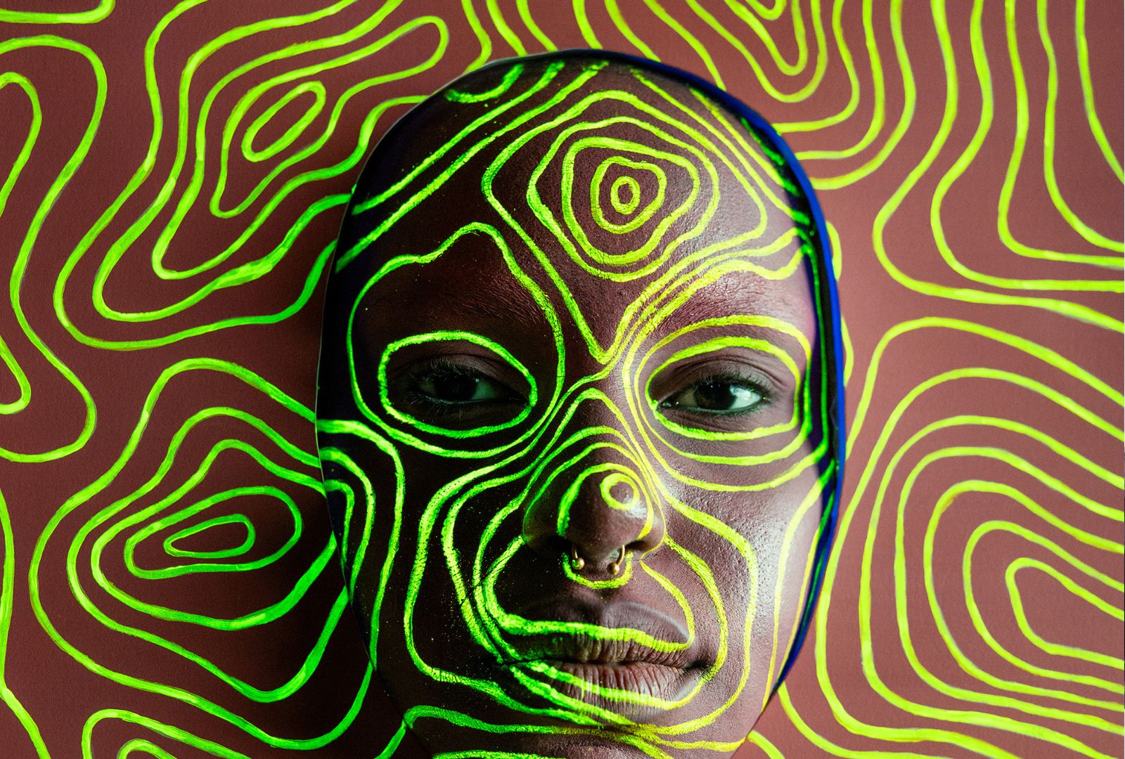 Green paint has been applied to a dark-skinned model and on a brown background in circular shapes, inspired by First Nations art.